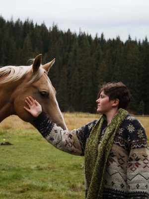 woman in black and green floral long sleeve shirt riding brown horse during daytime
